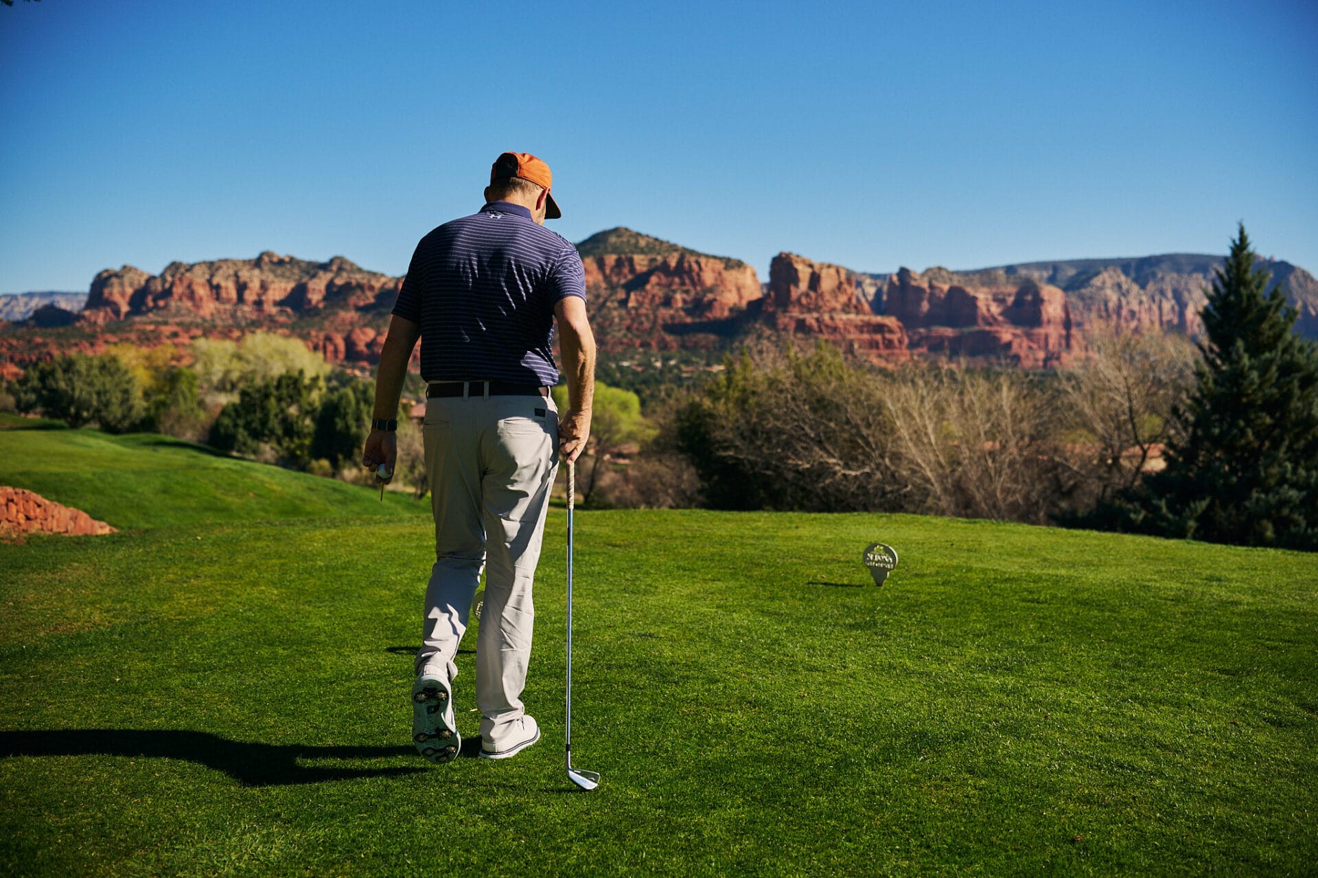 Golfer on a tee box at Sedona Golf Resort looking toward red rock formations under a clear blue sky.
