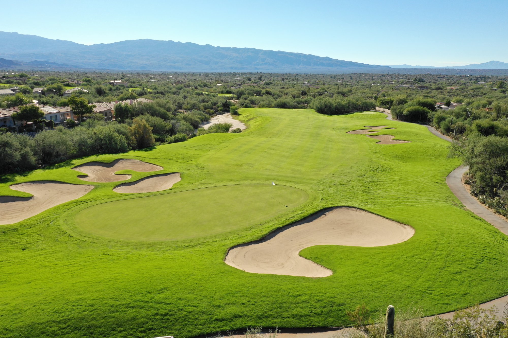 Aerial view of a desert golf hole at Arizona National Golf Club with green, bunkers, cart path, and mountains near Tucson.
