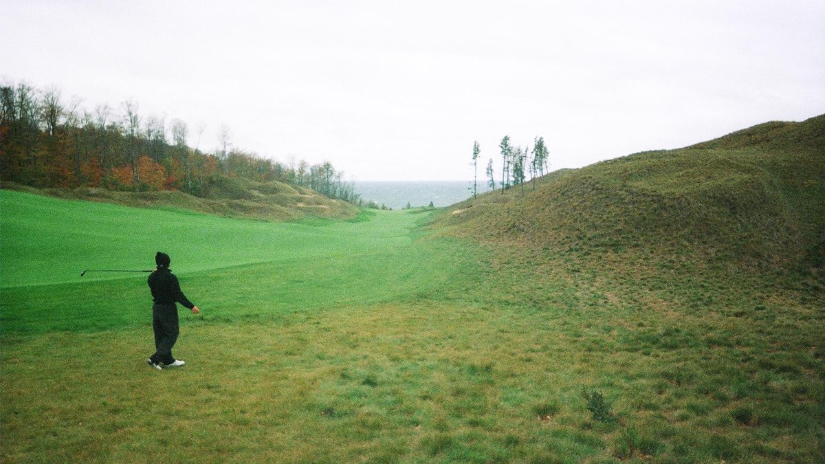 Golfer in the rough on the 11th hole at Arcadia Bluffs, with dunes and Lake Michigan beyond